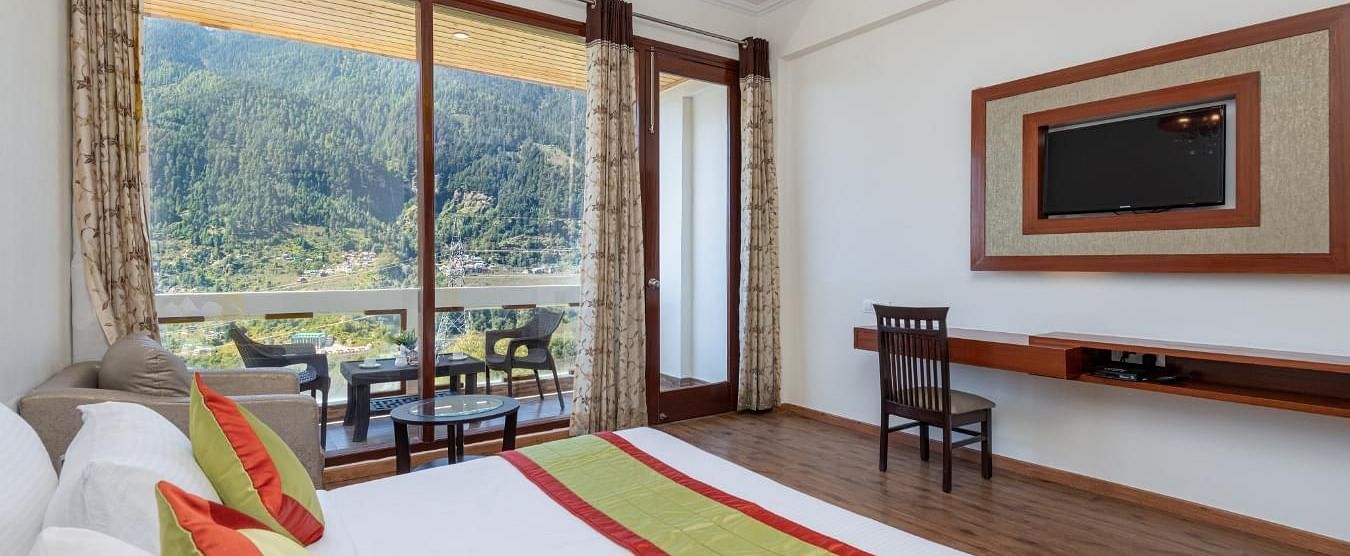 The photo displays a well appointed hotel room with a king size bed, plush bedding, and a cosy sitting area  | DLS Serenity Resort and Spa